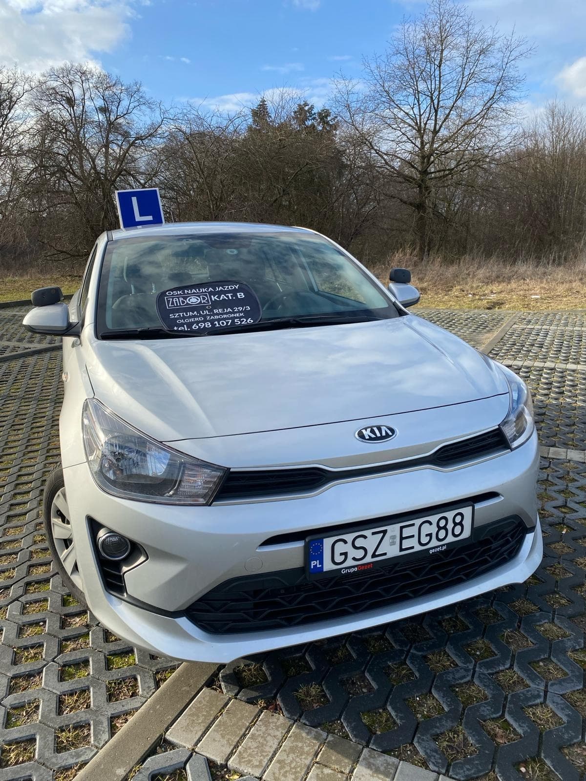 Srebrna KIA Rio z niebieskim oznaczeniem L, widok z przodu